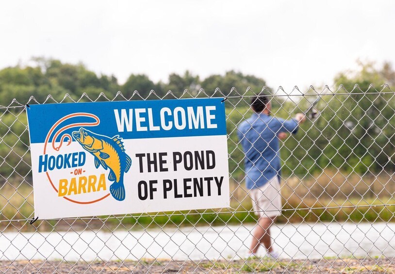 A man fishing behind a fence with a sign that reads 'Welcome to the Pond of Plenty.' 5