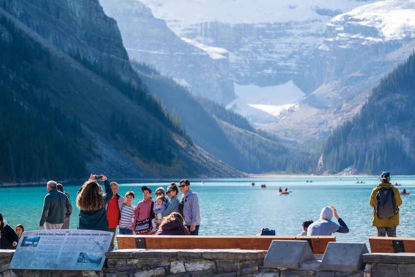A group of people at a lakeside viewpoint with mountains in the background. 1
