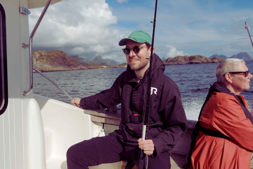 Two people on a boat with a rocky coastline in the background. 4