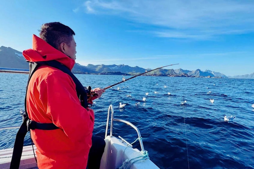 A person in a red jacket fishing on a boat with mountains in the background. 5