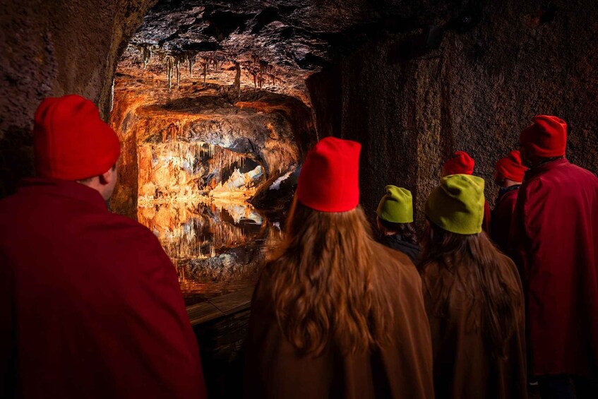 A group of people wearing red hats observing a cave interior with stalactites and a fire. 1
