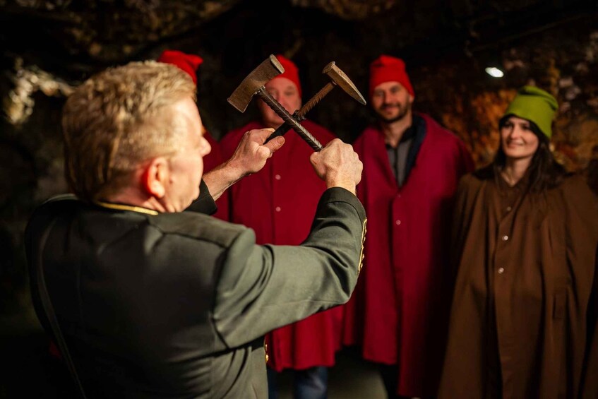 A person holding two large axes in front of a group of people in red coats. 3