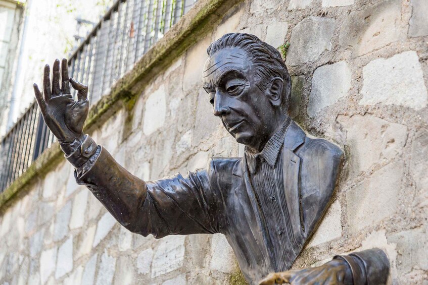 A bronze statue of a man with one hand raised against a stone wall. 3