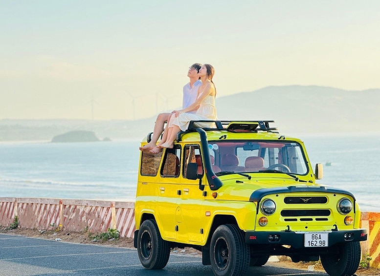 A yellow SUV parked by the roadside with a couple sitting on top. 1