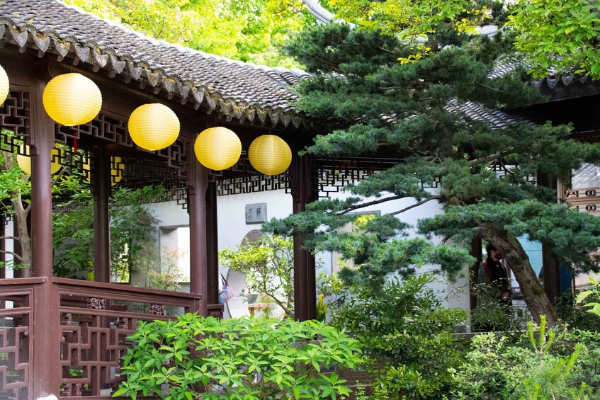 A traditional Japanese garden with a wooden pavilion, green foliage, and yellow paper lanterns. 2