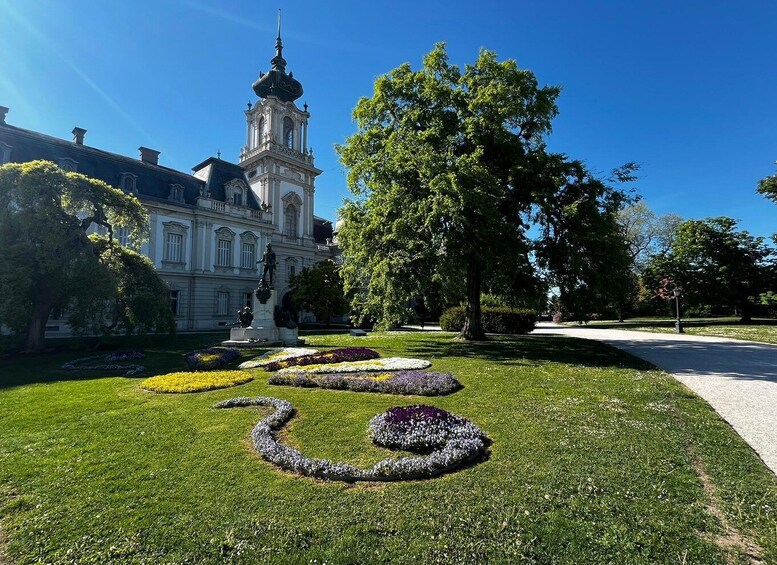 A formal garden with a statue, a large tree, and a building with a tower. 1