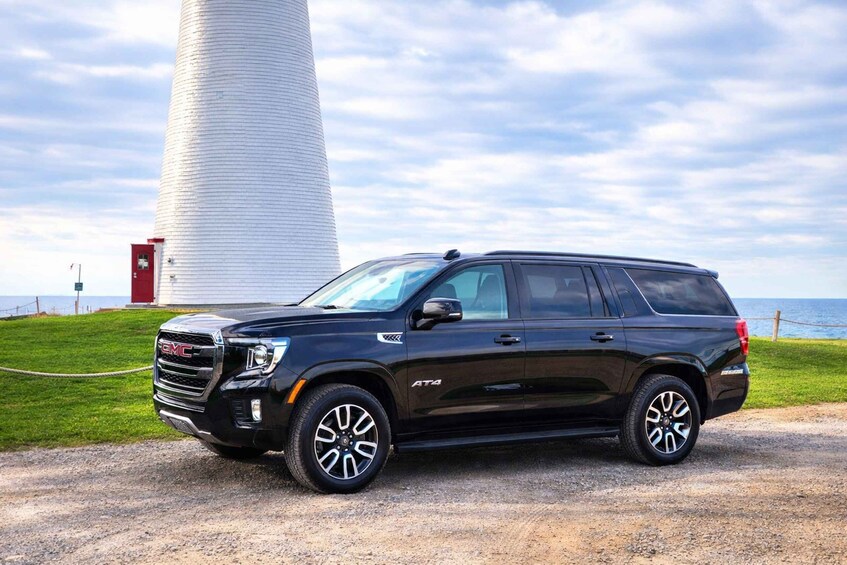 A black GMC Yukon SUV parked on a gravel path with a lighthouse and grassy area in the background. 1