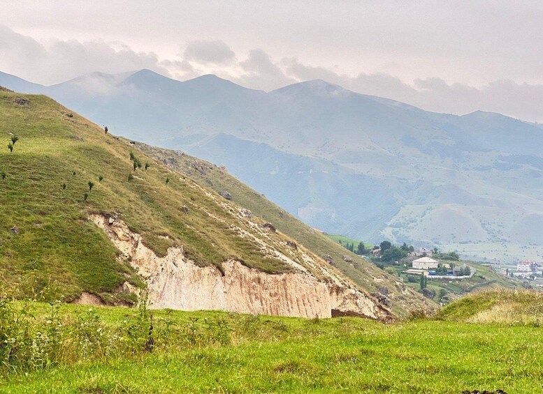 A mountainous landscape with a grassy slope, a rocky cliff, and a distant village. 2