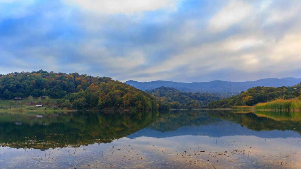 A calm lake with reflections, surrounded by autumn-colored trees and distant mountains. 4