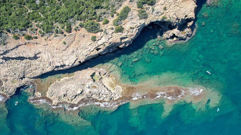 A rocky coastline with clear turquoise waters and a boat in the distance. 5