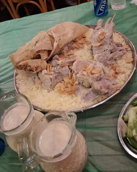 A meal with rice, meat, and almonds on a metal plate, with pitchers of a white liquid and a blue can in the background. 2