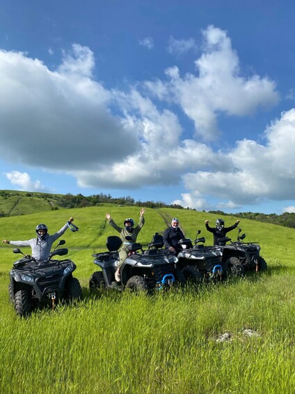 Four people on ATVs in a grassy field with a clear sky. 1