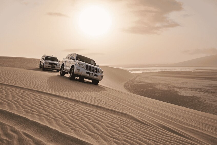 Two SUVs driving on a sand dune with a beach and ocean in the background. 4