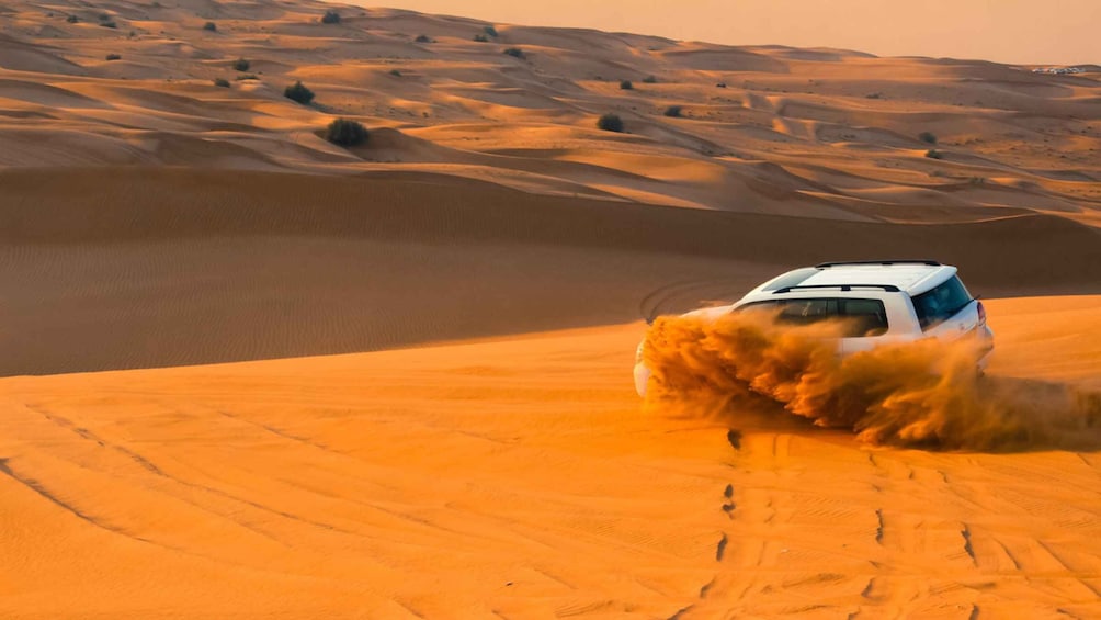 A white off-road vehicle driving through a desert with sand dunes. 5