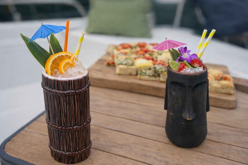 Two tiki drinks on a wooden table with a dessert tray in the background. 5