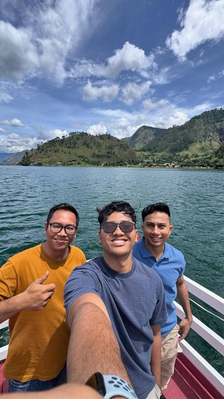 Three people on a boat with a lake and mountains in the background. 2