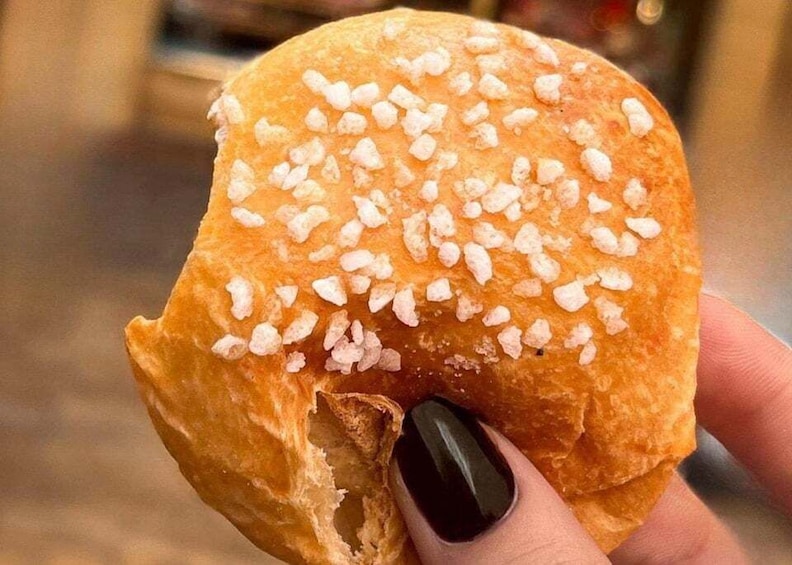 A hand holding a bread roll with sesame seeds on top. 4