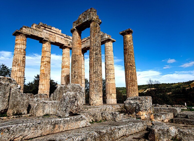 Ancient stone ruins with columns, including a partially collapsed structure, set against a clear blue sky. 1