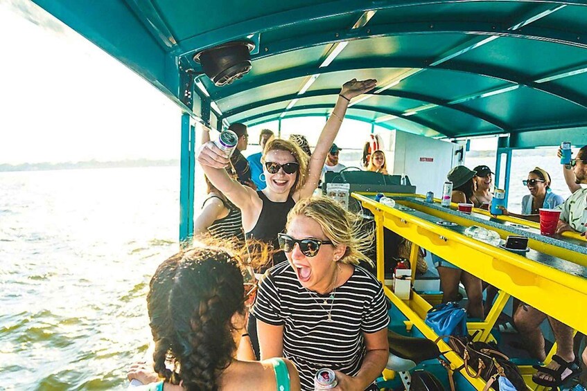 People on a boat with a blue canopy, holding drinks and taking photos. 3
