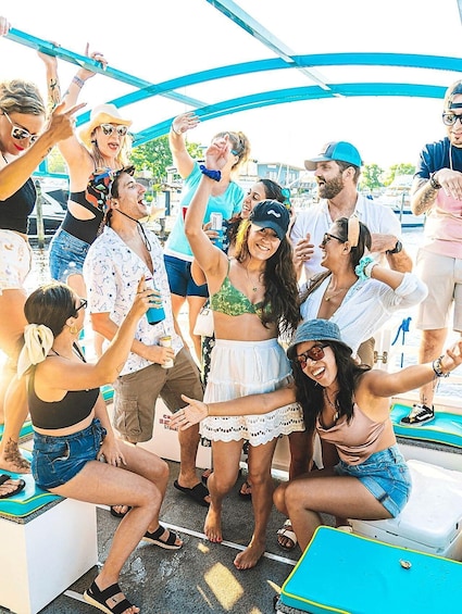 A group of people on a boat with a blue canopy, some holding drinks. 1