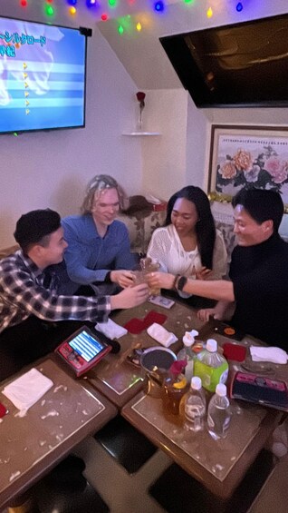 A group of people sitting around a table with drinks and a TV screen in the background. 3