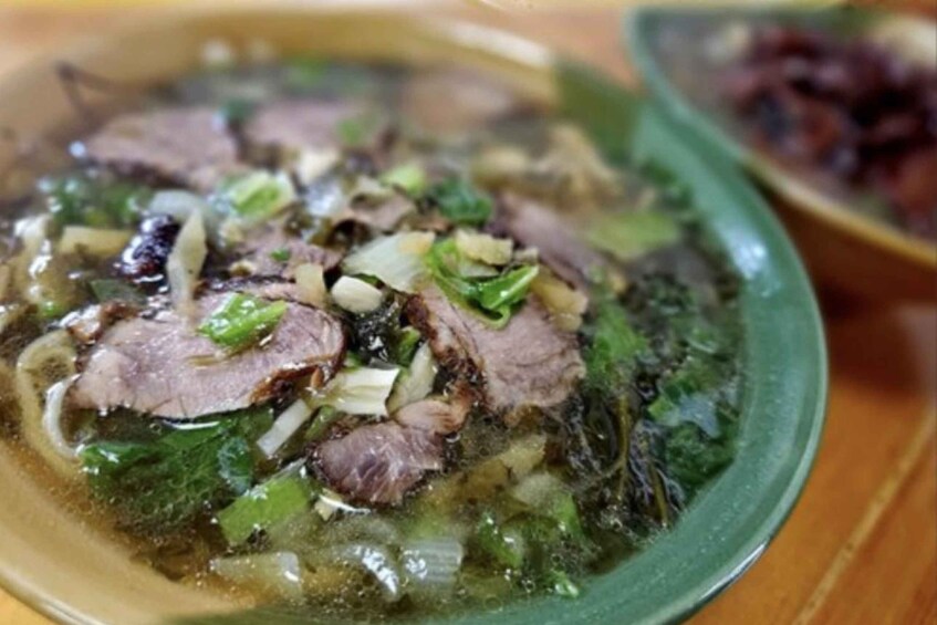A bowl of soup with meat and greens. 3