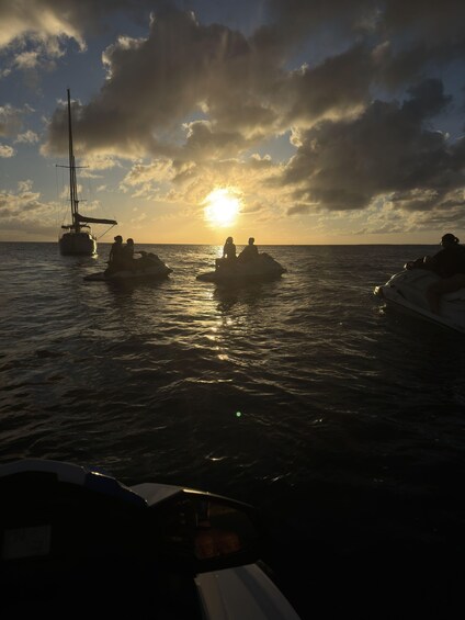 A sunset over the ocean with a sailboat and jet skis. 5
