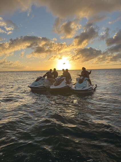 A sunset over the ocean with four people on jet skis. 1