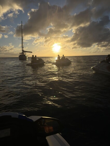 A sunset over the ocean with a sailboat and jet skis. 4