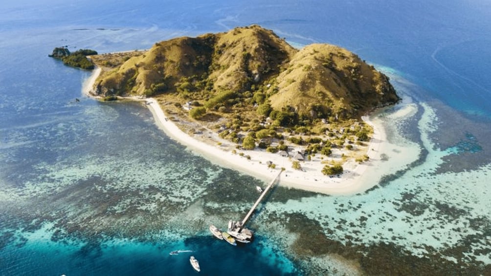 An island with a beach, clear waters, and a docked boat. 3