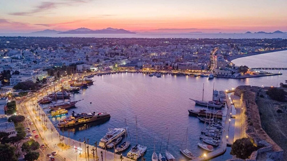 A coastal cityscape at dusk with a marina filled with boats, a prominent lighthouse, and a mountainous backdrop. 1