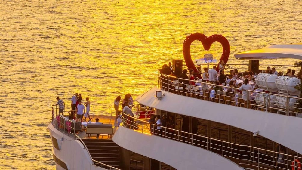 A cruise ship with a heart-shaped decoration on the deck, people dining, and the ocean in the background. 3