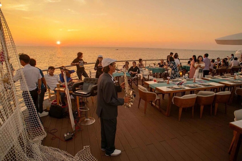 A sunset view from a deck with people dining and a saxophonist performing. 2