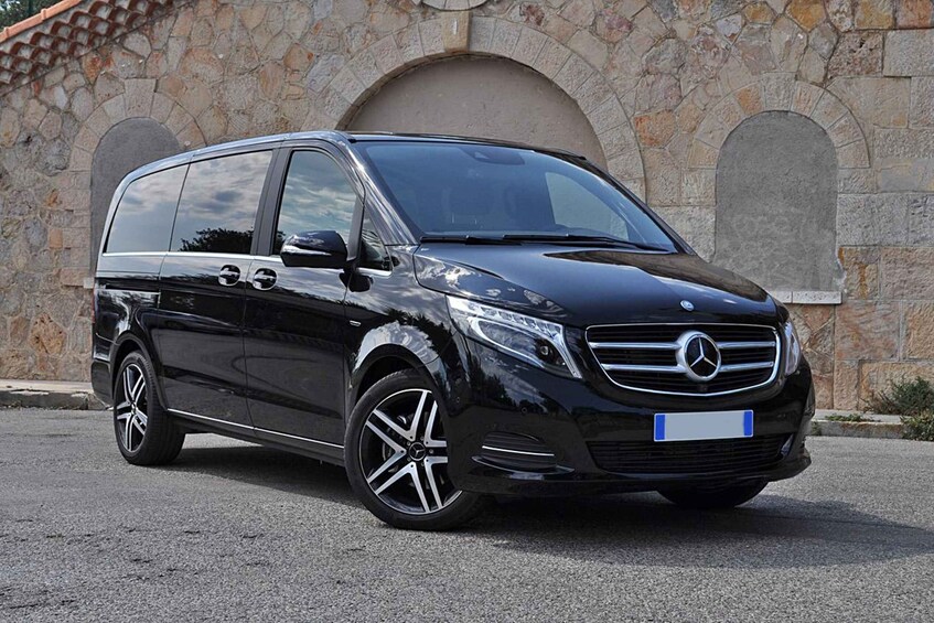A black Mercedes-Benz minivan parked in front of a stone building with arched windows. 5