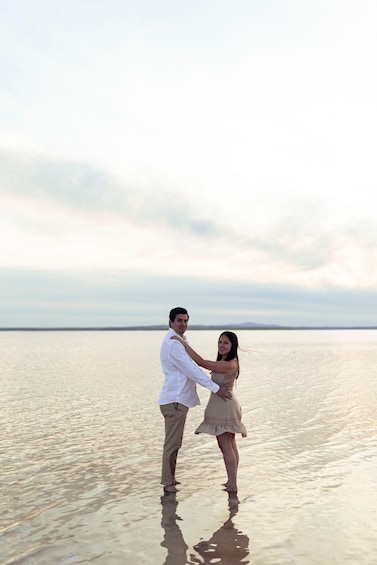 A couple standing in shallow water with a calm sea and overcast sky in the background. 4