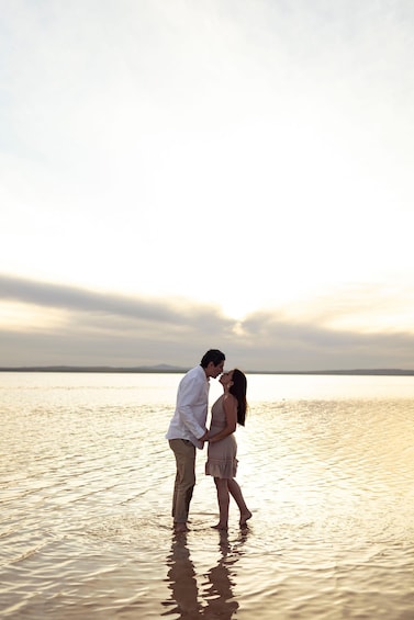 A couple standing in shallow water with a sunset in the background. 2