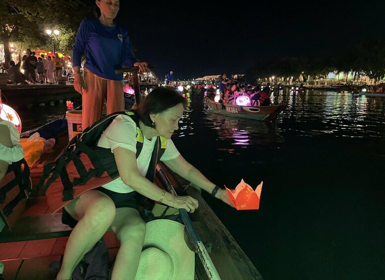 A person in a boat on a river at night with illuminated boats and a crowd on the shore. 2