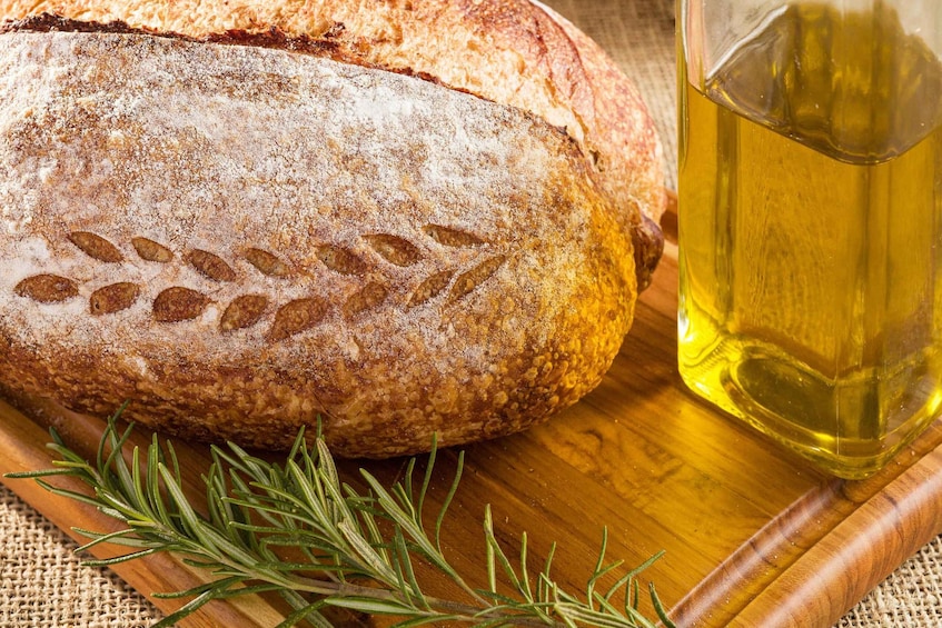 A loaf of bread with a rustic crust, a bottle of olive oil, and a sprig of rosemary on a wooden board. 2