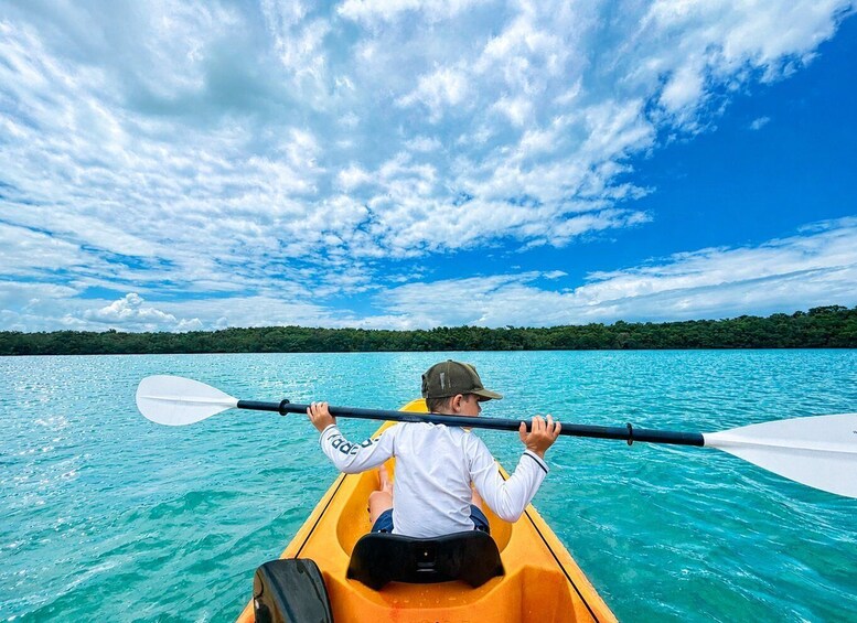 A person in a yellow kayak paddling on turquoise water with a forested island in the background. 3