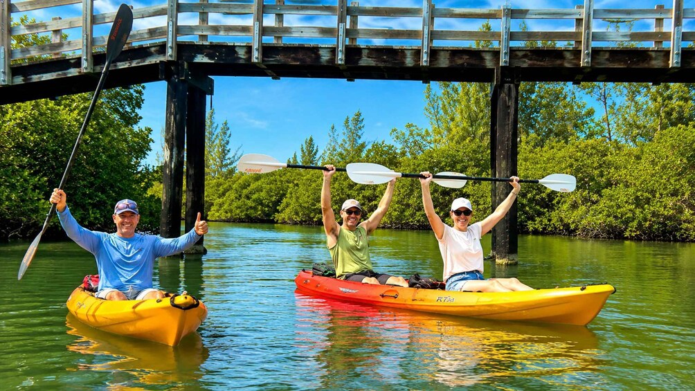 Two people kayaking under a bridge with a river and greenery in the background. 4