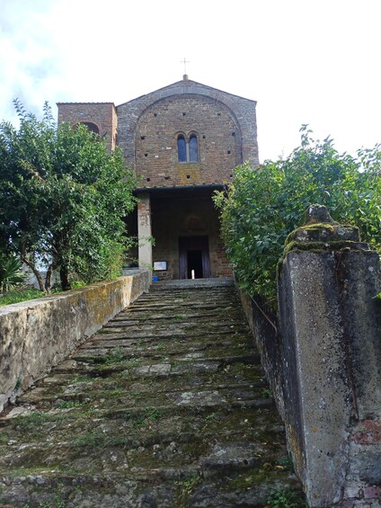 A stone staircase leading to a historic building with a cross on top, surrounded by greenery. 4
