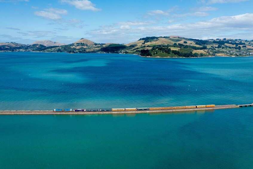 A coastal landscape with a train track extending into the water, surrounded by hills and a clear sky. 1