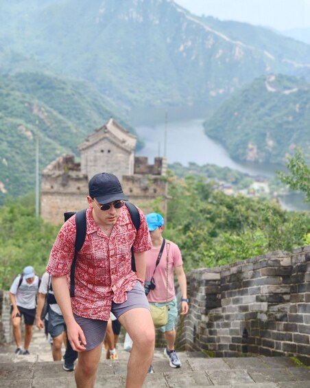 A person in a red patterned shirt and shorts walking on a stone path with a mountainous landscape and a body of water in the background. 5