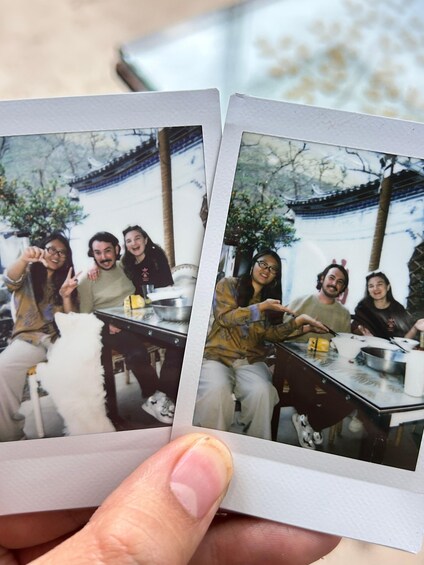 A person holding two Polaroid photos of a group dining outdoors. 1