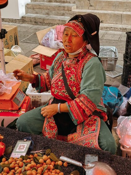 A person selling goods at a market stall, surrounded by boxes and baskets. 2