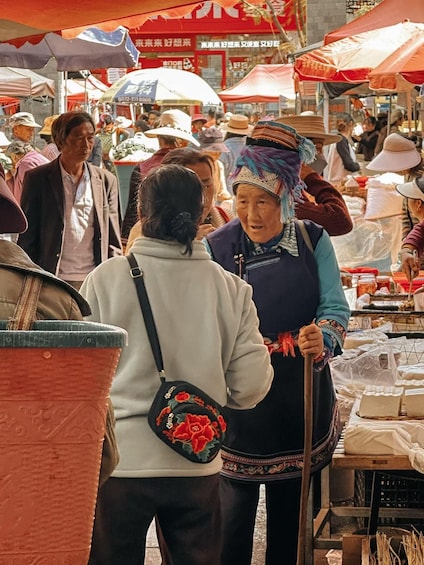 A bustling outdoor market with people shopping and vendors selling goods under red umbrellas. 5