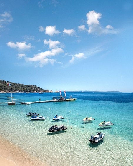 A clear blue sea with jet skis and boats anchored near the shore. 2
