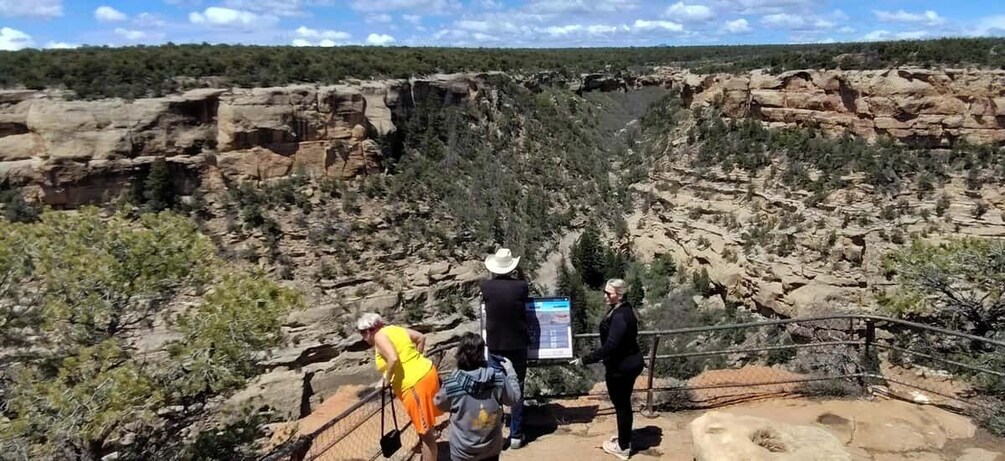 A rocky canyon with a viewing platform, a person in a yellow shirt, and another in a black jacket. 3