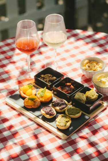 A table with a red and white checkered tablecloth, two glasses of wine, and an assortment of appetizers. 4