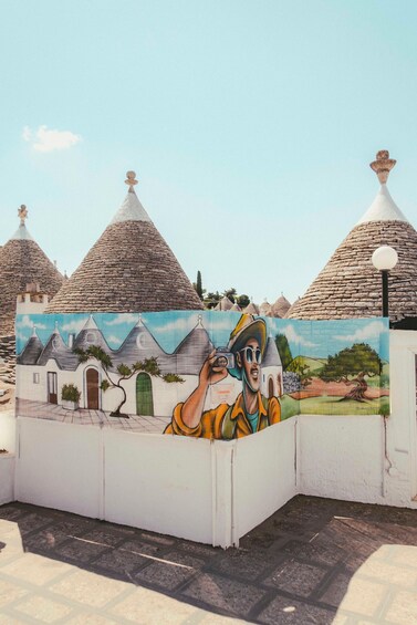 A mural of a village with conical roofs and a person taking a photo. 5